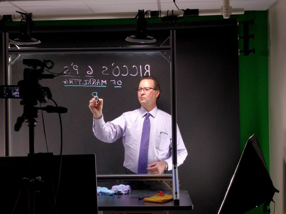 Professor using lightboard with camera filming them